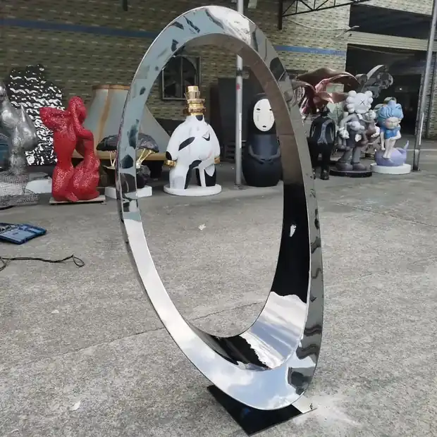 Freestanding abstract sculpture in a plaza with reflective surface catching light