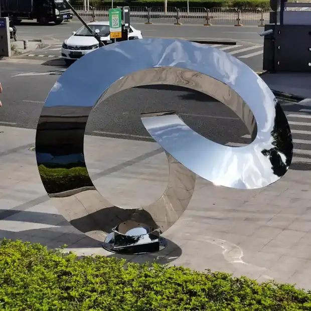 Large abstract sculpture with mirror finish reflecting surrounding building lines
