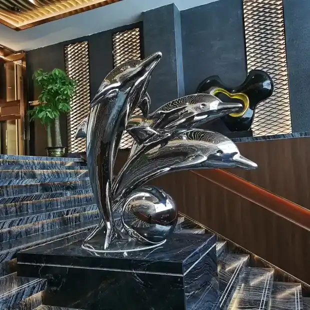 Stainless steel dolphin sculpture in mirror polish reflecting sky and trees