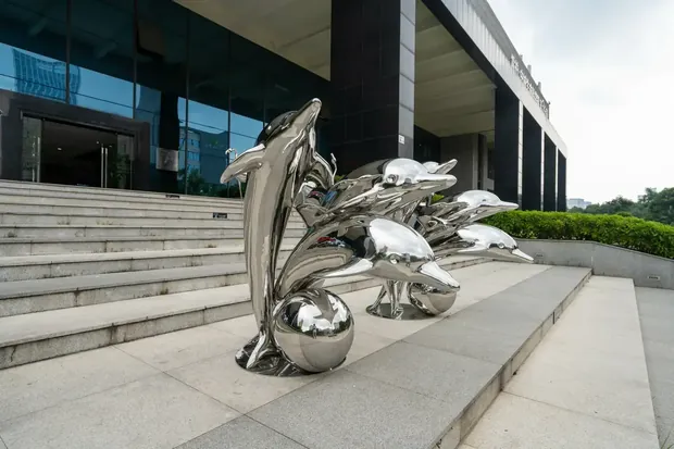Stainless steel dolphin sculpture in a hotel entrance courtyard with natural light