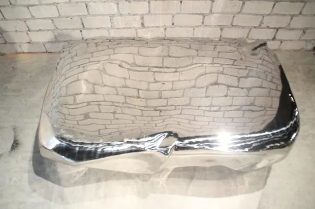 Sculptural stainless steel coffee table with mirror polish in a modern living room