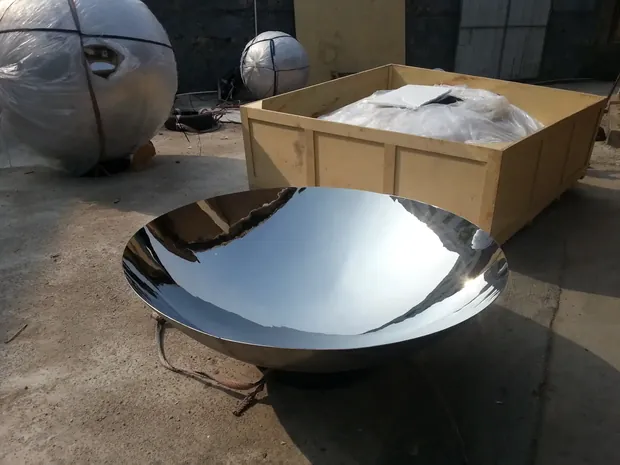 Concave and convex stainless steel mirror sculptures on a wall, reflecting sky and surroundings