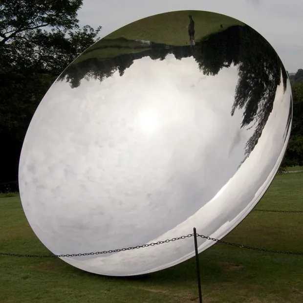 Group of concave mirrors arranged in a garden courtyard with planting around