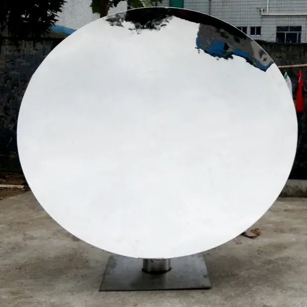 Concave mirror sculpture placed in a public plaza with people walking nearby