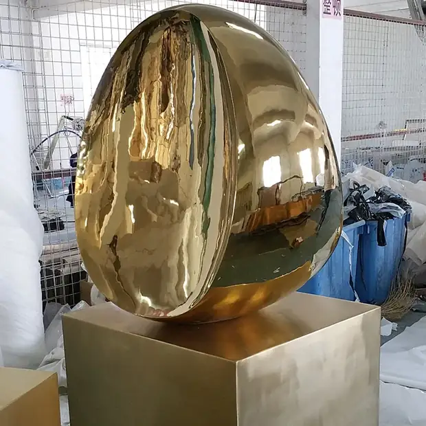 Gold egg-shaped sculpture on a gold pedestal in a workshop.