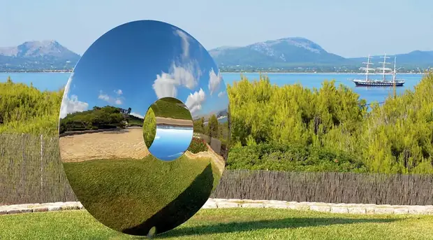 Large stainless steel sculpture reflecting sky and trees in a public park setting