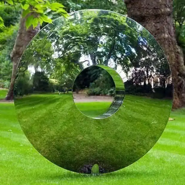 Mirror polished stainless steel sculpture in the form of an eye, standing in a garden landscape