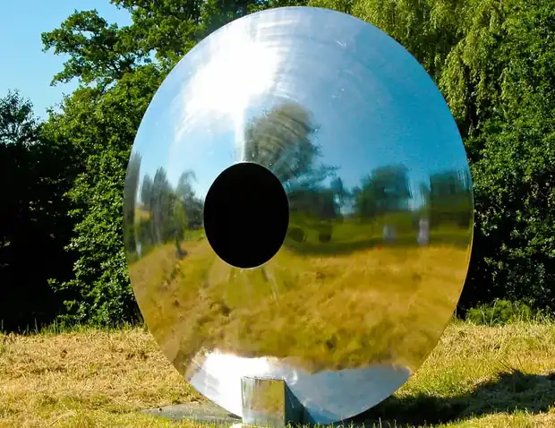 Angled view of a stainless steel eye sculpture in a modern garden design