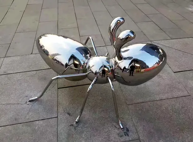 Giant stainless steel ant sculpture standing in a public park landscape