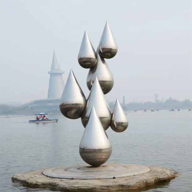 Stainless steel droplet sculpture under overhead lighting with light reflection