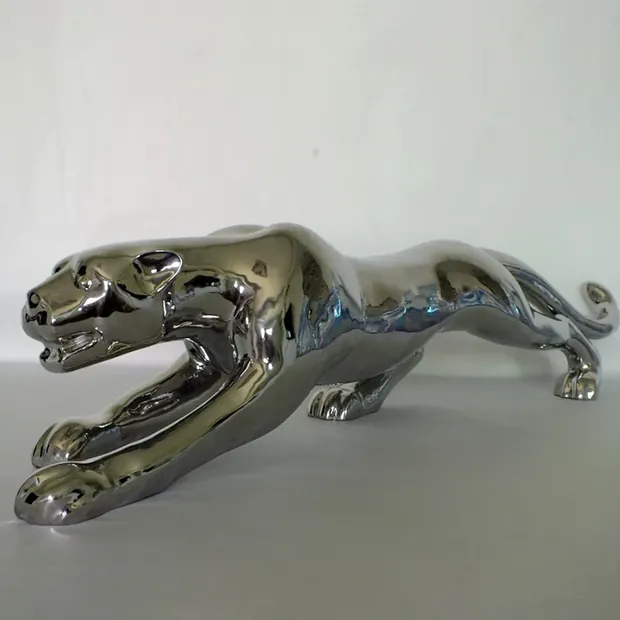 Stainless steel leopard sculpture in a park plaza, reflecting the sky and surrounding trees