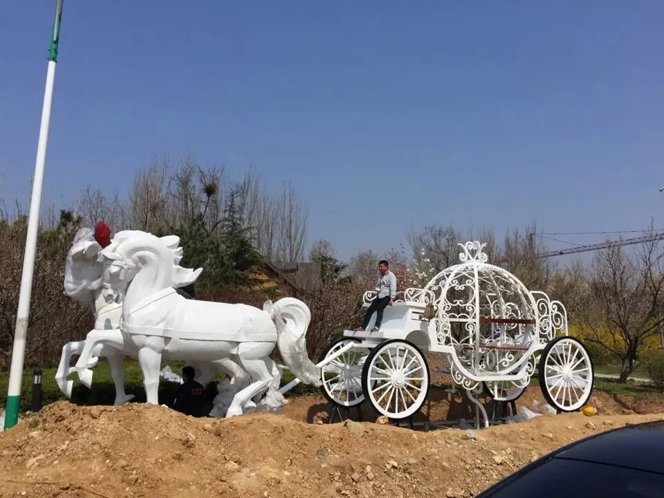 Stainless steel carriage sculpture in a park setting with reflective surface catching the sky
