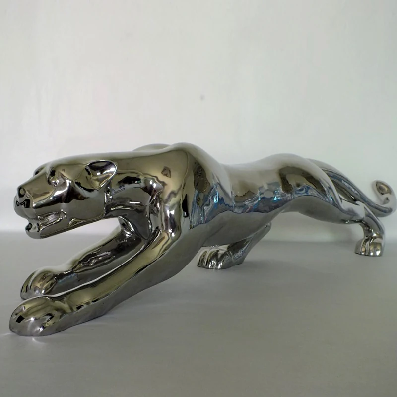 Stainless steel leopard sculpture in a park plaza, reflecting the sky and surrounding trees