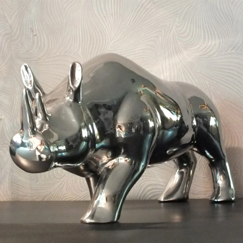 Stainless steel rhino sculpture on a wooden desk with a reflective surface
