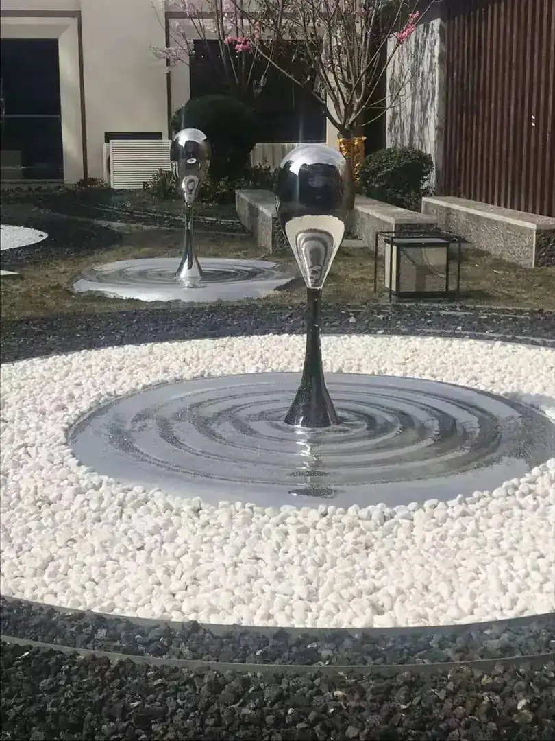 Stainless steel water drop sculpture with overlapping forms on a wall