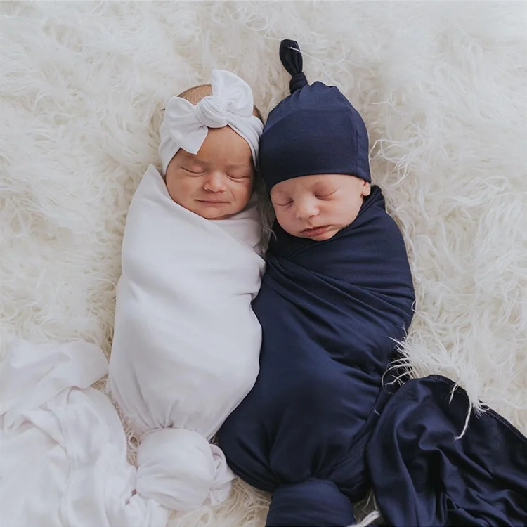 Swaddle blanket folded into a square with headband and hat placed beside it