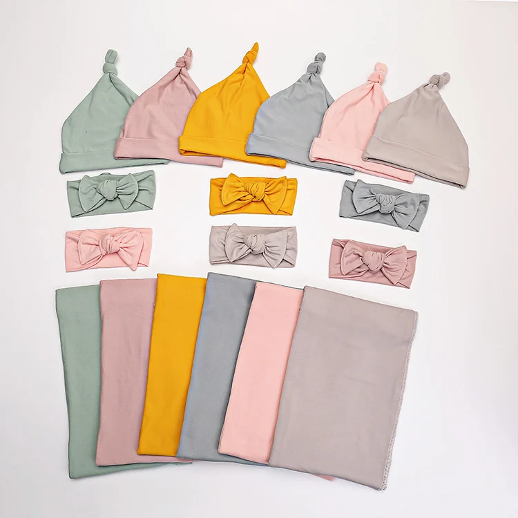 Pink 80*80cm muslin swaddle blanket with headband and hat laid out on a white surface
