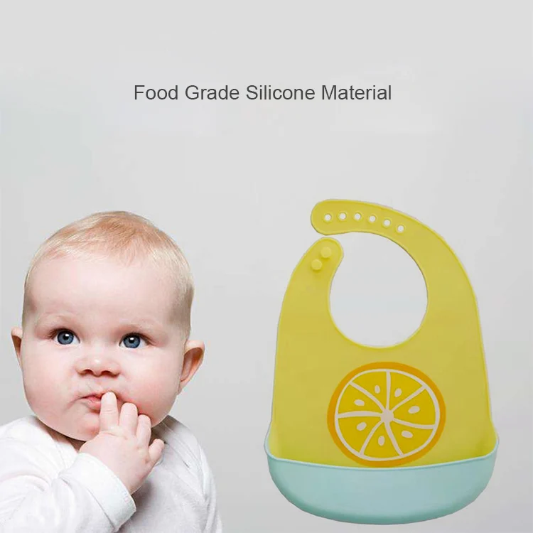 White silicone baby bib placed on a table with a spoon and food in the pocket