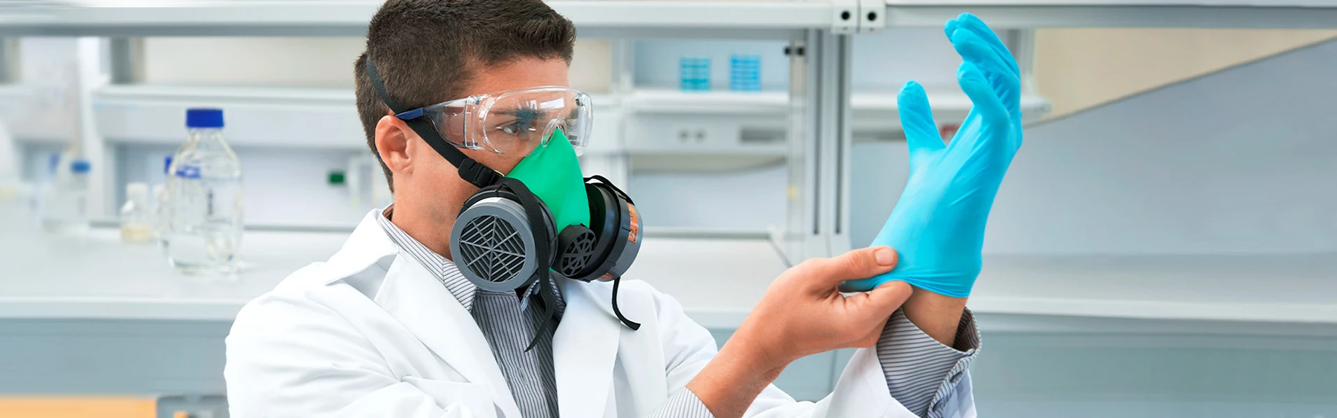 A technician in a respirator holding a nitrile examination glove