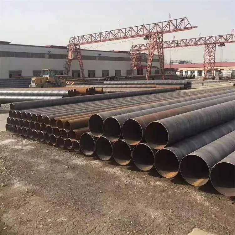 Large rusty steel pipes stacked in a yard beneath a gantry crane