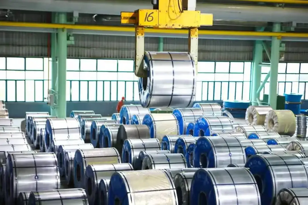 Rows of wrapped galvanized coils beneath a yellow overhead crane