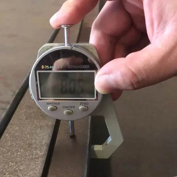 Digital thickness gauge held against the edge of a steel plate