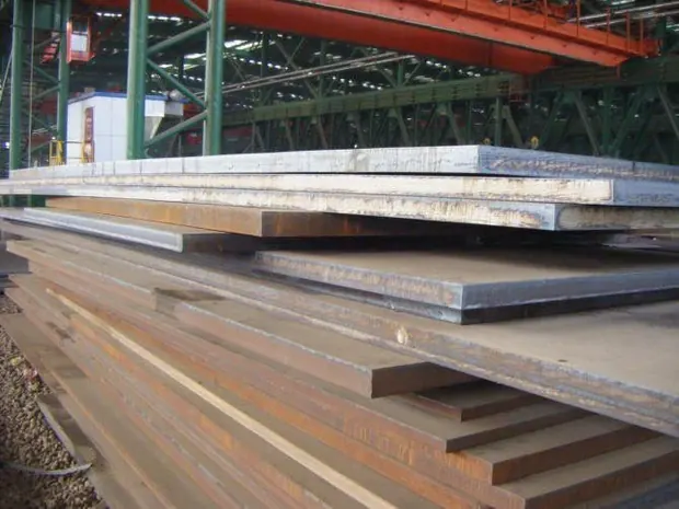 rust surfaced steel plates stacked in a mill bay under a crane