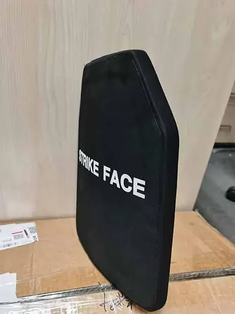 black curved armor plate propped on cardboard packaging