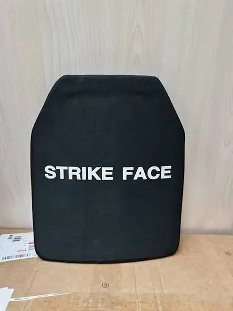 black armor plate standing upright against a pale wall