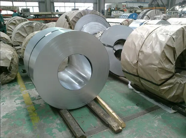 large bright steel coil lying on a warehouse floor beside more coils