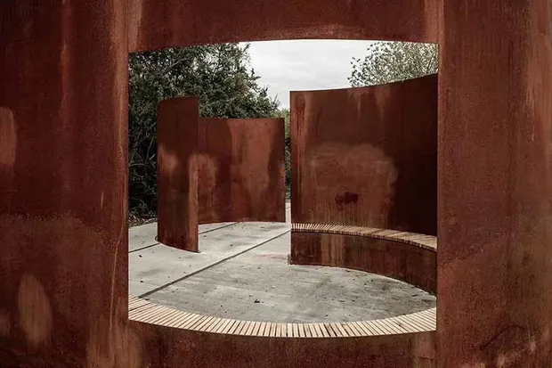 rusted corten steel sculpture with a large circular opening outdoors