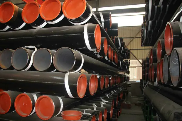 Steel pipes with orange plastic end caps stacked indoors