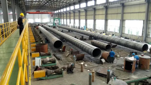 Worker on a walkway beside rows of large diameter welded pipes