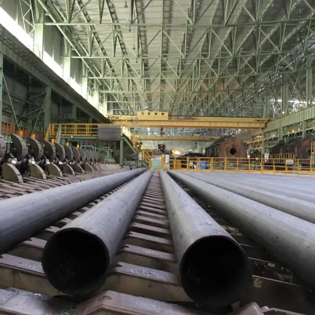 Large-diameter steel pipes laid out in a crane-served factory hall