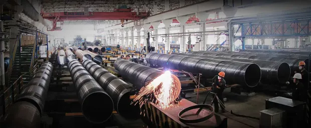 Sparks flying as workers weld rows of large steel pipes