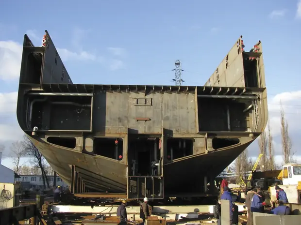 Large welded steel hull block section outdoors with workers nearby