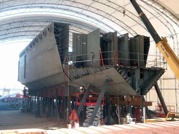 Barge hull under construction on blocks inside a shipyard shed