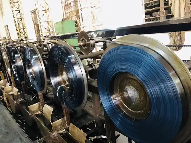 Blue tempered steel strip coils on a slitting machine in a workshop