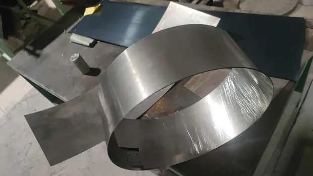 Loose loop of bright steel strip beside flat sheets on a bench