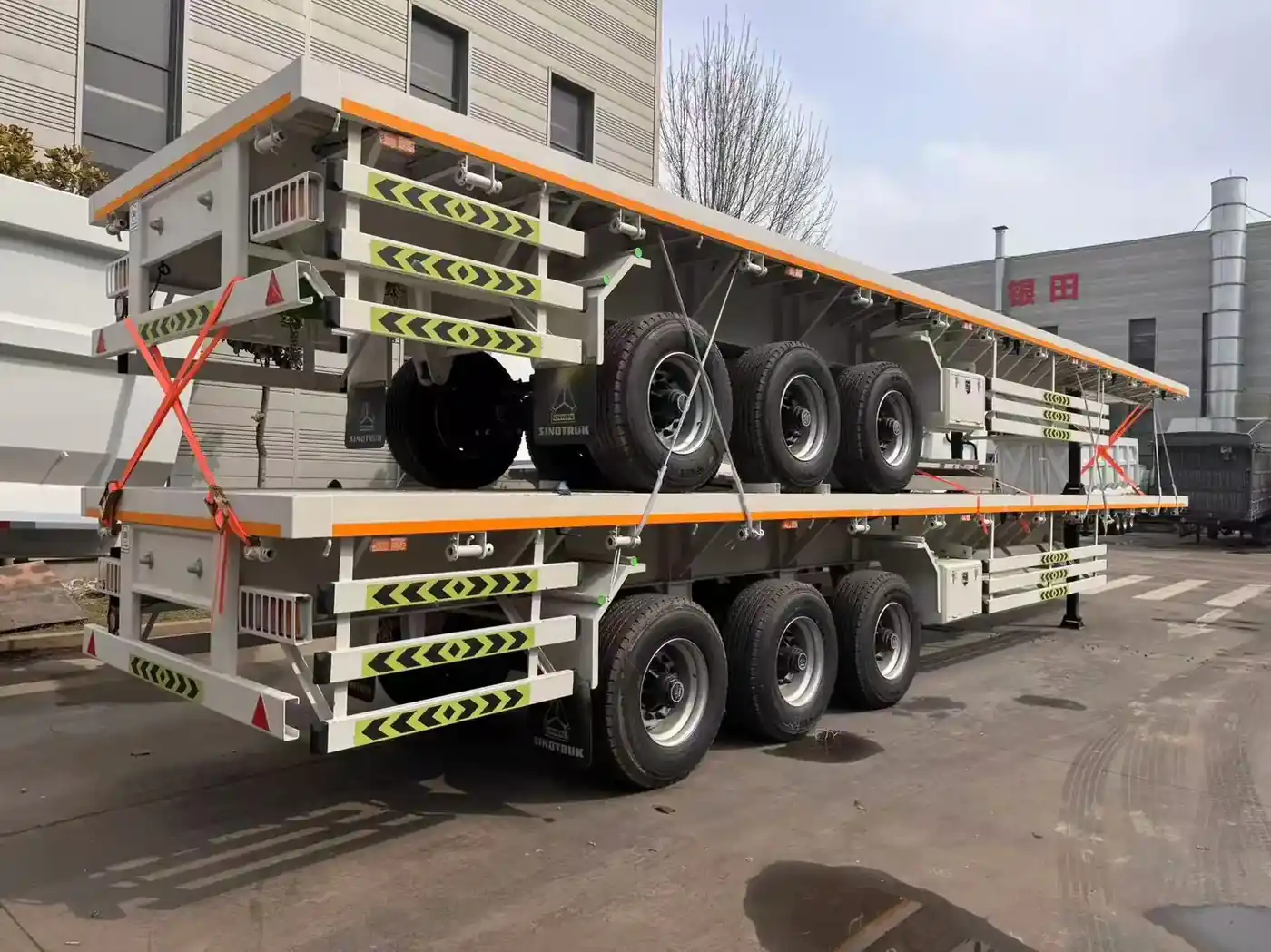 Two finished flatbed semi trailers parked outside the SINOHENG production hall ready for dispatch