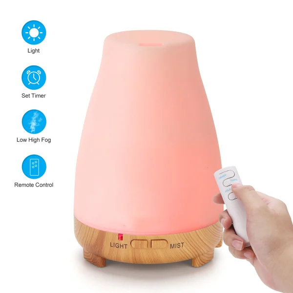 Aroma diffuser glowing pink with wood-grain base, hand holding white remote control, feature icons at side