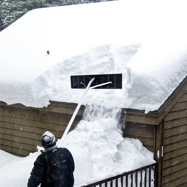 Person using a long-handled snow rake to clear a thick layer of snow from a roof.
