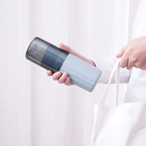 Person holding a grey travel toothbrush cup case with translucent lid next to a white tote bag