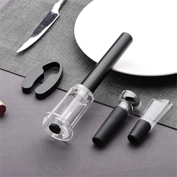 Set of four air pressure wine bottle opener components, including a black pump handle, clear vacuum chamber, foil cutter, and pourer, arranged on a gray surface near a white plate and knife.