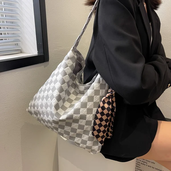 Model in a black blazer carrying a grey and white checkerboard canvas shoulder bag with a small checkered scarf accent