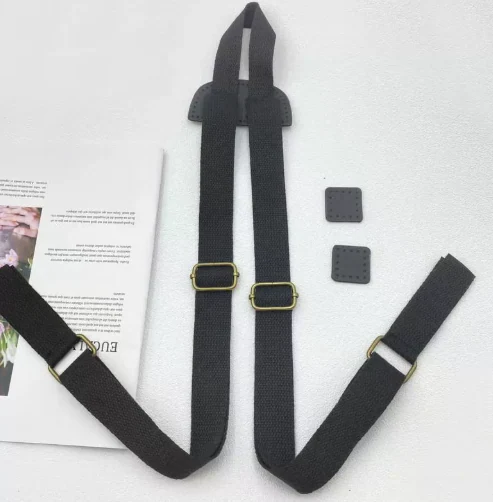 Black backpack straps with brass slider buckles and small leather pads laid flat on a white surface beside a magazine