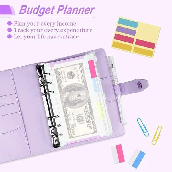 Purple budget planner binder open with a $100 bill in a cash envelope, surrounded by label stickers and a pen.