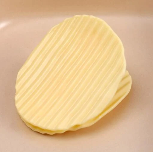 Yellow ridged potato chip shaped bag sealing clip resting on a smooth pink surface