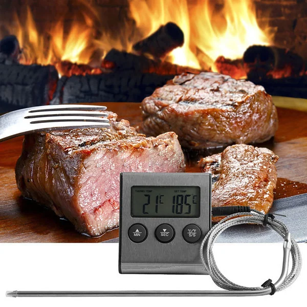 Digital meat thermometer with probe displayed in front of cooked steaks and a fireplace.
