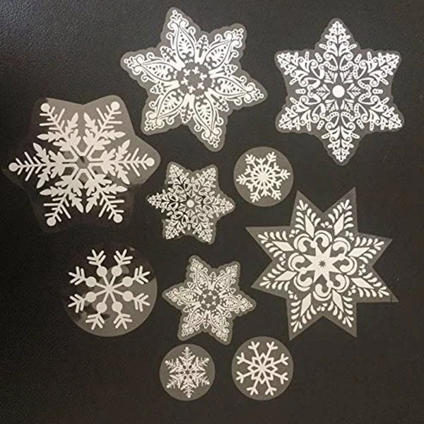 Assorted white snowflake electrostatic window stickers in various sizes arranged on a dark background.
